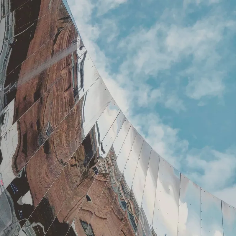 A curved mirrored sculpture reflecting brick buildings and blue sky