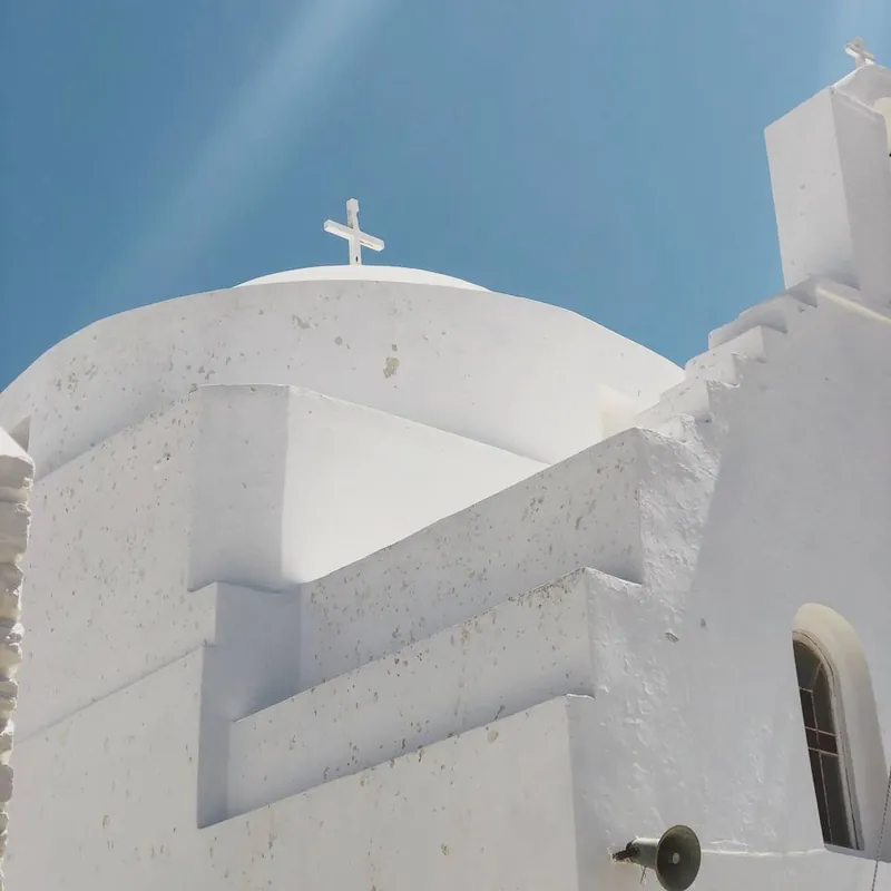 A whitewashed church dome with a cross against a deep blue sky
